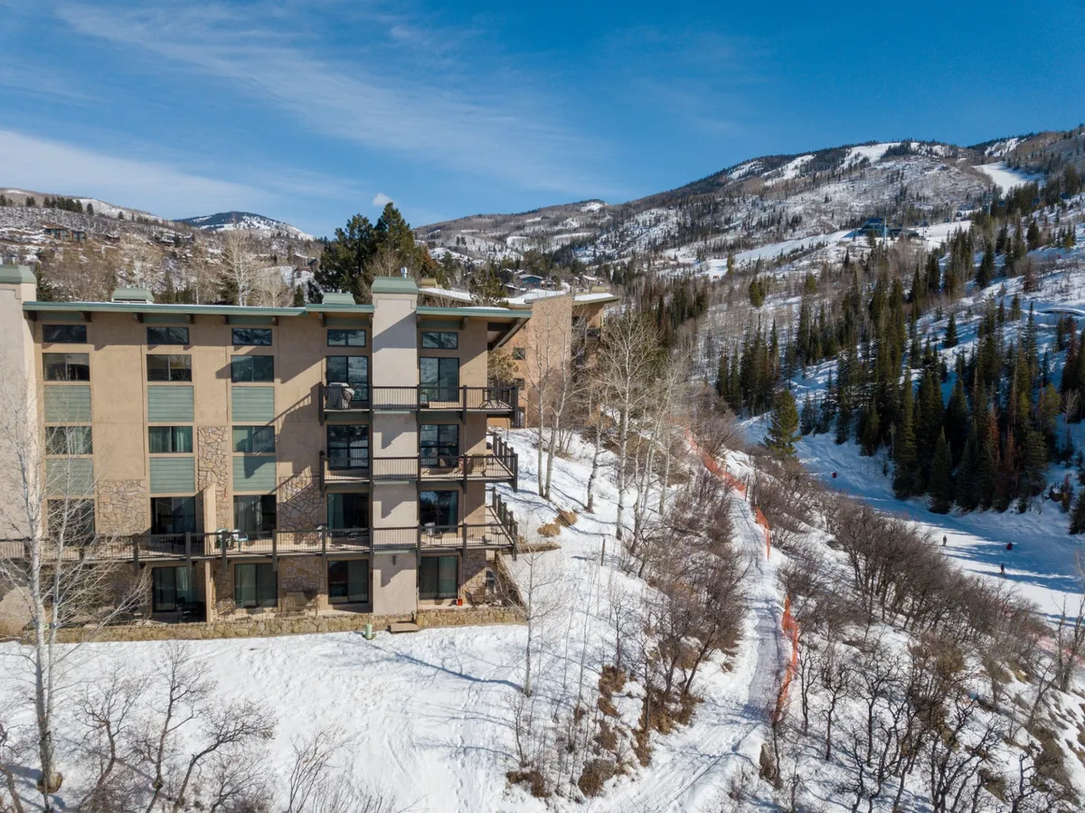 A wide view of the building's architecture set against a dramatic, snow-covered mountain backdrop. The surrounding area is serene, ideal for those seeking adventure and relaxation in a scenic setting.