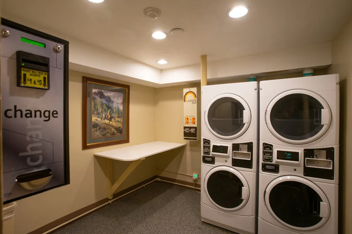 The shared laundry room is depicted here, with multiple laundry machines and a change machine, set against the backdrop of some subtle artwork. The space appears clean and accessible.