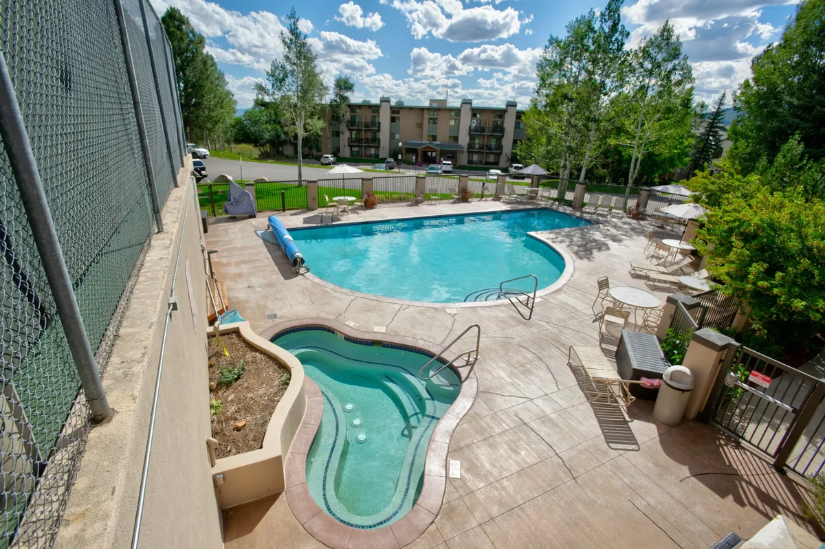 This exterior image features a large swimming pool and adjacent hot tub, framed by lush greenery and a comfortable seating area. The area is inviting for both active swimmers and those looking to relax on the loungers. The space is designed for both group gatherings and quiet afternoons, exemplifying the resort-style recreation described in the section.