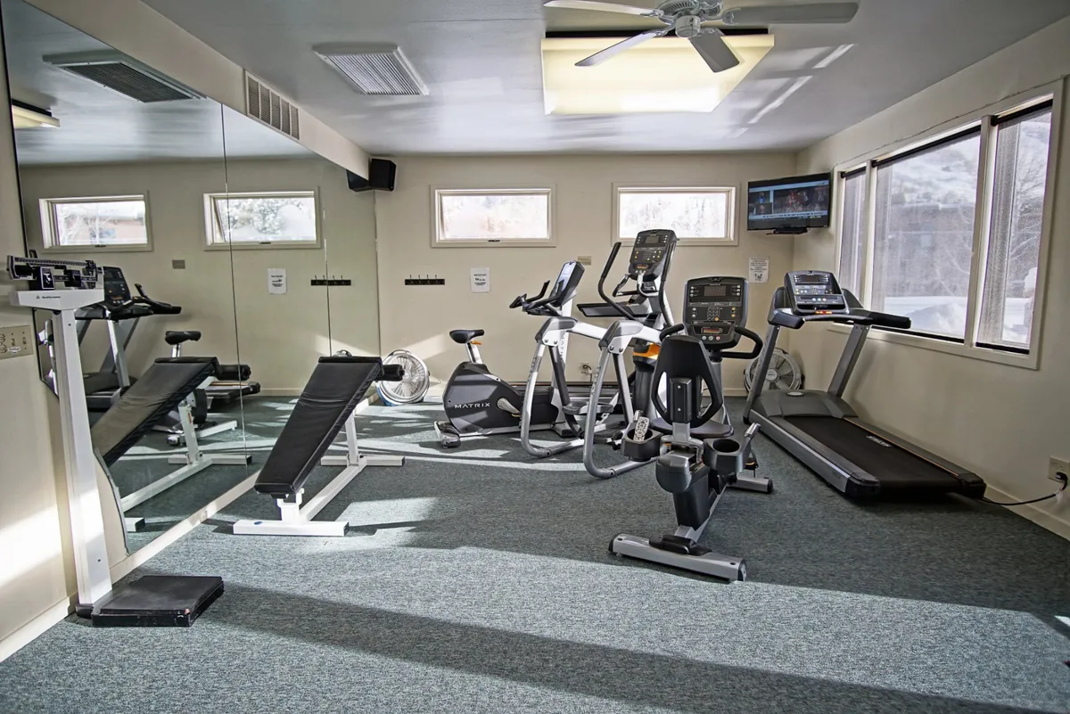 This interior shot showcases a modern fitness center with a treadmill, stationary bike, and weight bench in front of a mirror. The equipment is spaced out in a clean, bright room suitable for both solo and group workouts, underscoring the active lifestyle opportunities available at the property.