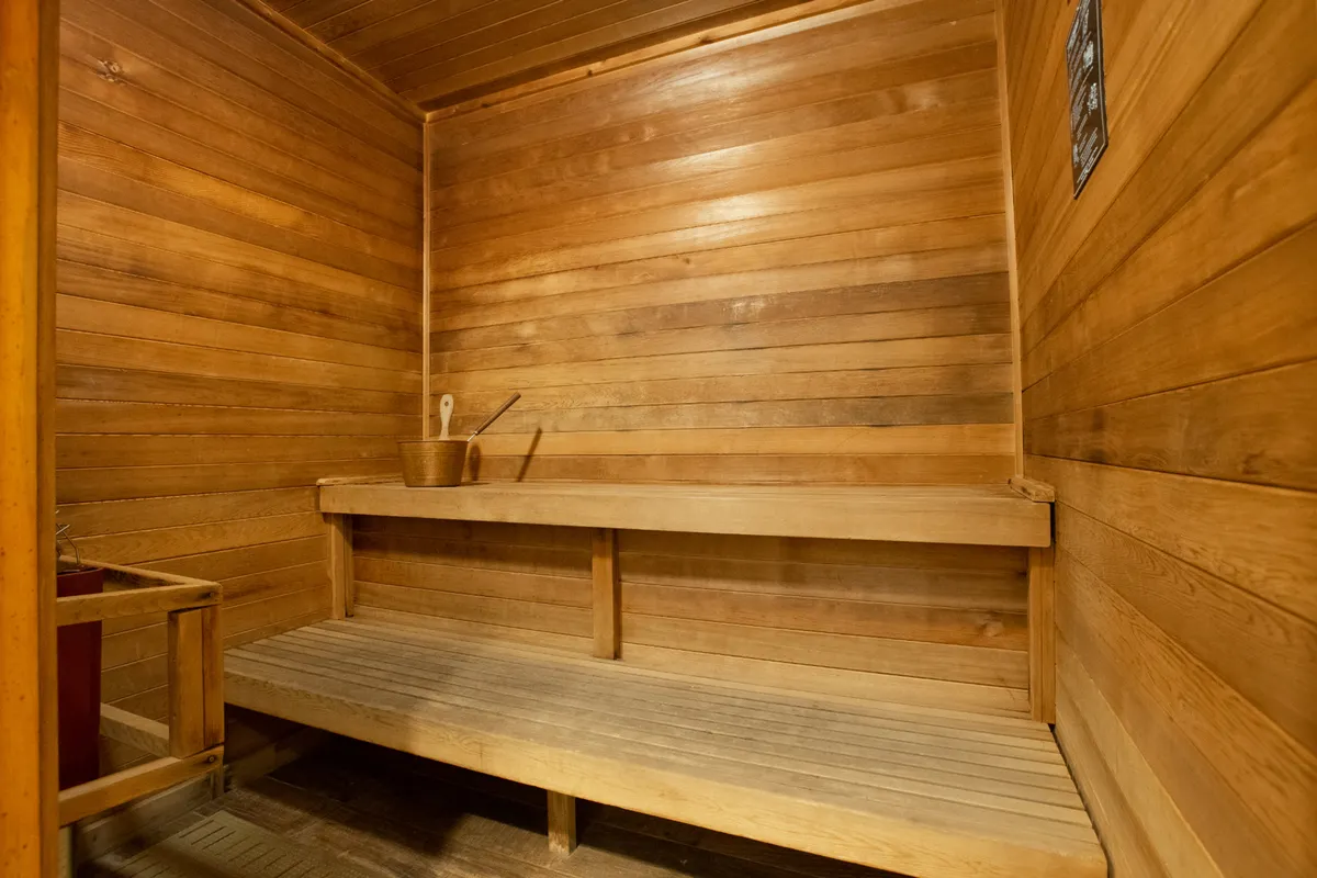 This cozy interior image captures a wooden sauna room with benches and a classic bucket and ladle. The warm wood tones and inviting layout evoke a sense of comfort and deep relaxation—ideal for unwinding after a workout or a day outdoors.