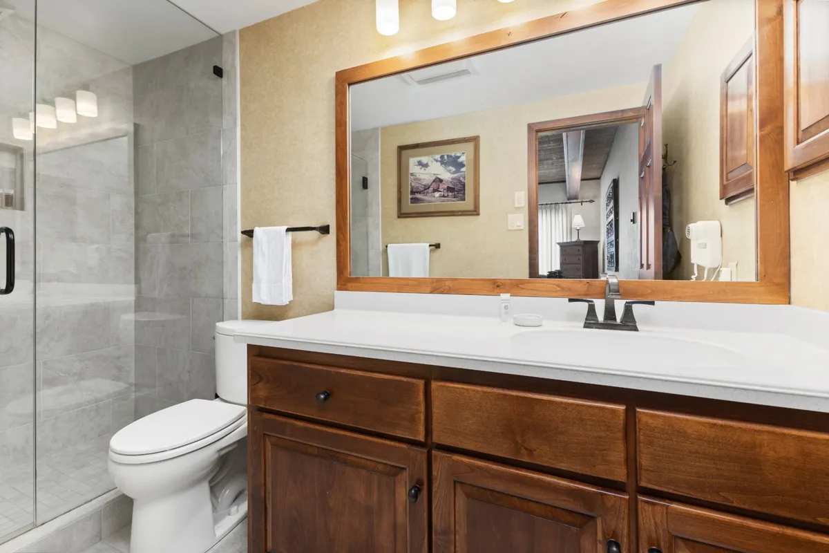 A fresh, modern bathroom with a wooden vanity, large mirror, and glass shower enclosure. The inviting atmosphere is ideal for personal care and relaxation after a day of mountain adventures.