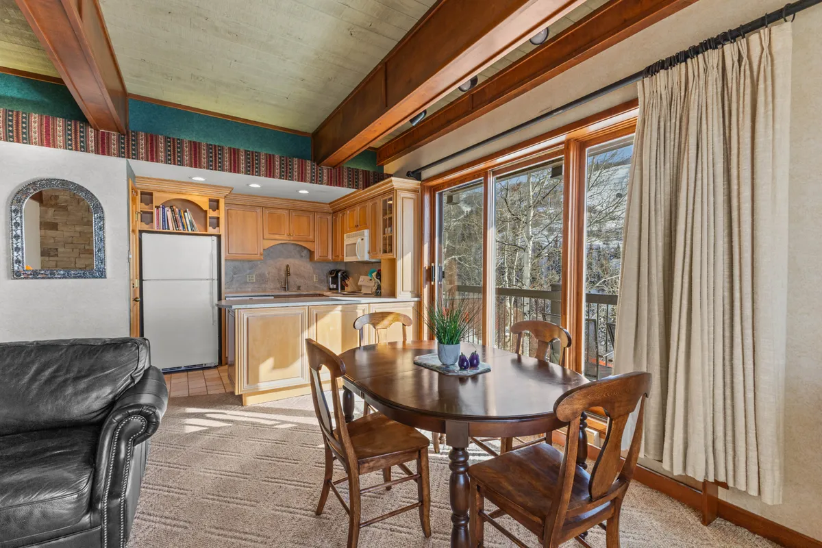 This image shows a welcoming open-plan living and dining area, featuring a dining table, a kitchen area with modern appliances, large windows that let in natural light, and a comfortable leather sofa. The layout is practical and inviting, ideal for family meals, casual gatherings, and relaxing after arrival.