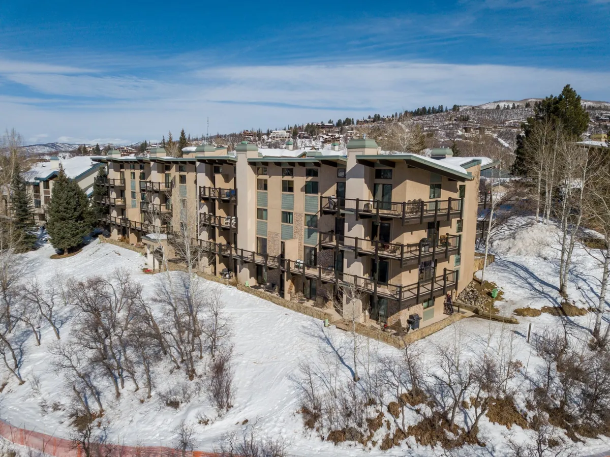 This image features the building's facade with several balconies overlooking a snow-covered ground and surrounded by trees. The tranquil winter setting is welcoming, suggesting a cozy retreat with immediate access to nature and outdoor activities.